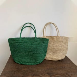 May include: Two woven tote bags. One is a vibrant green, the other a natural beige. Both have sturdy handles and a spacious design. The bags are made of a textured material, perfect for carrying essentials. Ideal for shopping or a day at the beach.