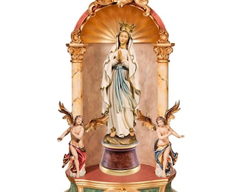 Op de afbeelding: Religieus beeld van de Maagd Maria, gekroond en gekleed in het wit, in een sierlijke gouden en marmeren nis. Twee engelen flankeren het beeld. De basis is groen en goud.