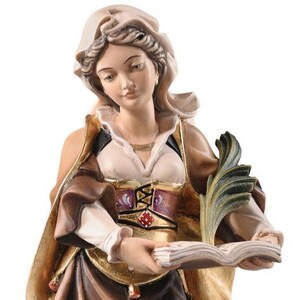 May include: A detailed figurine of a woman in a historical outfit, holding a book and a decorative leaf. The figure is painted with a variety of colors, including gold, brown, and white. The figurine has a detailed face and is wearing a head covering.