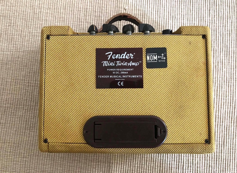 Puede incluir: Un amplificador de guitarra Fender Mini Twin-Amp con un exterior de tweed amarillo. El amplificador tiene un asa de cuero marr&oacute;n, perillas de control negras y un compartimento de bater&iacute;a rectangular marr&oacute;n. Una etiqueta marr&oacute;n dice "Fender Mini Twin-Amp".