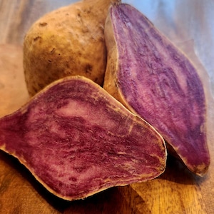 May include: Three sweet potatoes, two are cut in half and show a vibrant purple flesh with white streaks. One sweet potato is whole and has a brown skin.