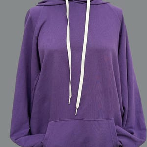 May include: A purple hooded sweatshirt with white drawstrings. The sweatshirt has a kangaroo pocket.