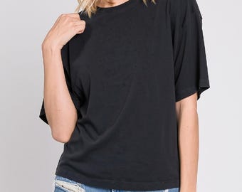 Könnte beinhalten: Ein einfarbiges schwarzes T-Shirt mit kurzen Ärmeln, Rundhalsausschnitt und lockerer Passform, kombiniert mit hellblauen Jeansshorts, die ausgefranste Kanten und sichtbare Risse auf den Vorderteilen aufweisen, was einen strukturierten Look erzeugt.