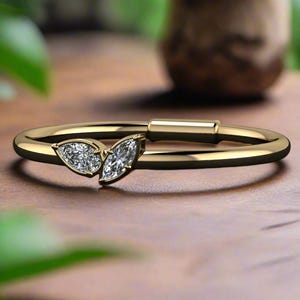 Könnte beinhalten: Ein zarter Goldring mit zwei birnenförmigen Diamanten, die in einem schlichten Band gefasst sind.