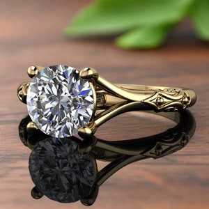 Puede incluir: Un anillo de compromiso de oro con un gran diamante redondo y claro. El anillo tiene un diseño delicado y adornado con una banda dividida.