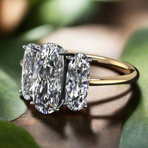 May include: A three-stone oval engagement ring with a gold band. The center stone is larger than the two side stones.