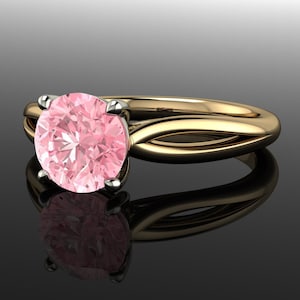 May include: A gold ring with a pink gemstone set in a prong setting. The band is twisted and has a polished finish.