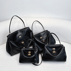May include: Four black leather handbags of varying sizes are displayed. Each bag features a structured design with a top handle, a gold-colored clasp, and a front pocket. The bags are arranged on a white, curved surface.