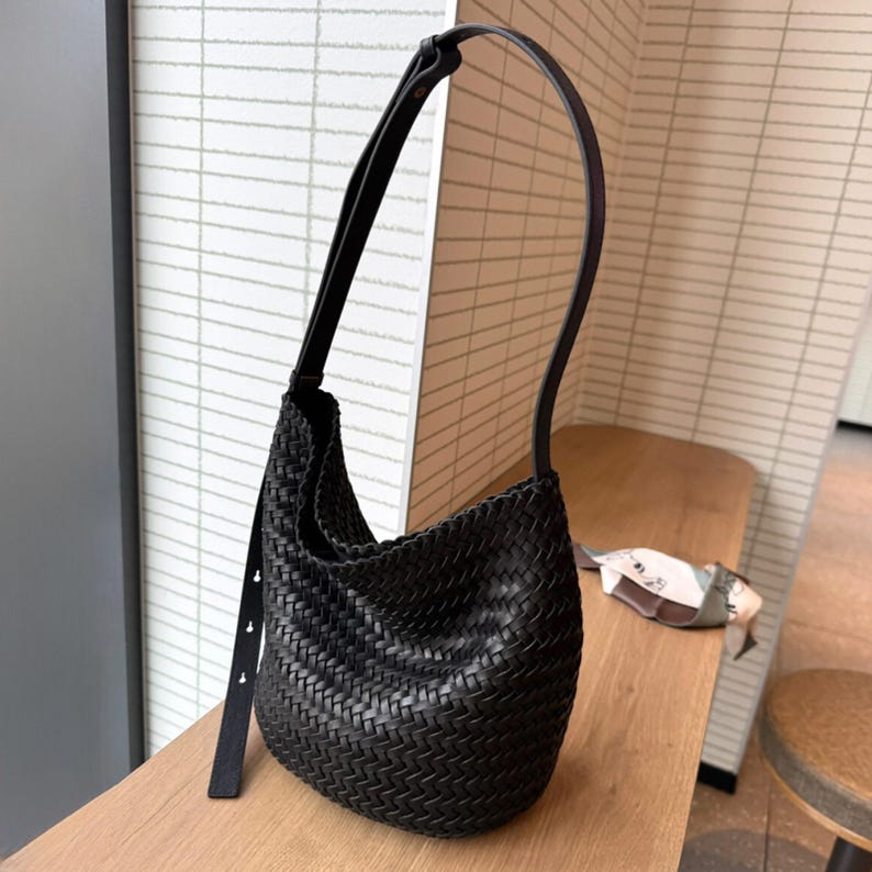 May include: A black woven leather shoulder bag with a long strap. The bag has a curved shape and a braided design.