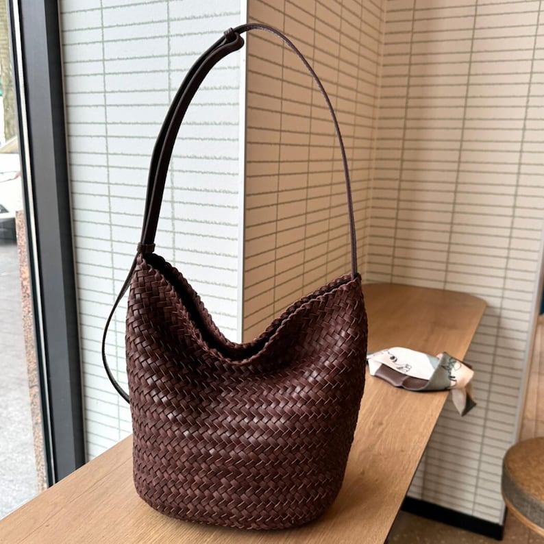 May include: A brown woven leather shoulder bag with a long strap. The bag is made of a thick, woven leather and has a slouchy, casual look.
