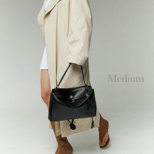 May include: A black leather handbag with a flap closure and a silver-tone clasp. The bag has a top handle and a long shoulder strap. The word "Medium" is visible in the image.