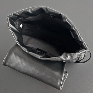 May include: Black leather handbag with an open top, revealing a spacious interior. The bag features a woven design on the side and a flap closure. The bag is shown against a dark background.