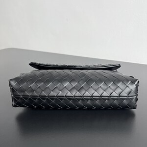 May include: A black leather clutch with a woven pattern. The rectangular bag has a flap closure and a textured surface. The bag is sitting on a black surface.