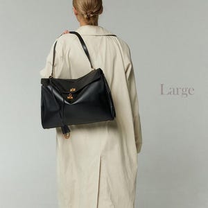 May include: A large black leather handbag with a flap closure and gold-colored hardware. The bag has a long shoulder strap and a tassel detail. The word "Large" is printed in a light purple color on the right side of the image.