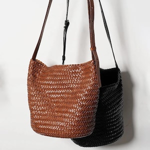 May include: Two woven leather shoulder bags, one brown and one black. The bags have a bucket shape and are made with a braided leather design.