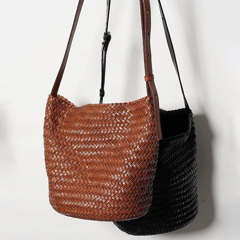 May include: Two woven leather shoulder bags, one brown and one black. The bags have a bucket shape and are made with a braided leather design.