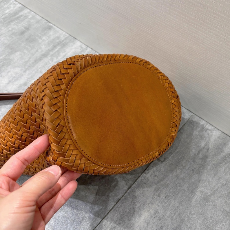 May include: A brown woven leather bucket bag with a round bottom. The bag is made of a braided leather design.