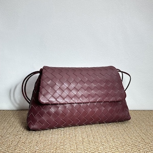 May include: A burgundy leather clutch with a woven design. The bag has a flap closure and thin shoulder straps. The clutch is made of a soft, pliable leather and is a deep, rich color.