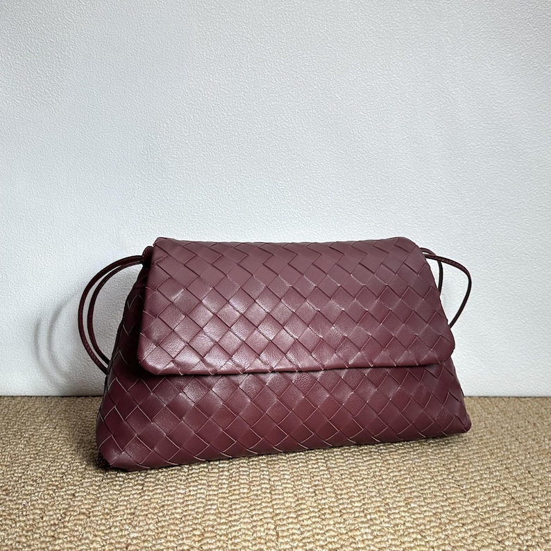 May include: A burgundy leather clutch with a woven design. The bag has a flap closure and thin shoulder straps. The clutch is made of a soft, pliable leather and is a deep, rich color.