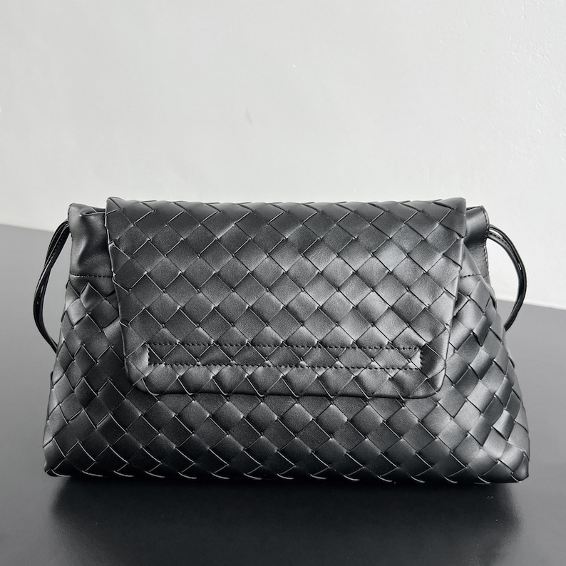 May include: A black woven leather clutch with a flap closure. The bag features a repeating diamond pattern and a thin strap on each side. The clutch is rectangular and appears to be made of high-quality leather.