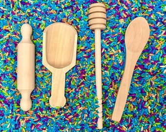 May include: Four wooden kitchen tools on a bed of colourful rice. The tools include a rolling pin, a small scoop, a honey dipper, and a spoon.