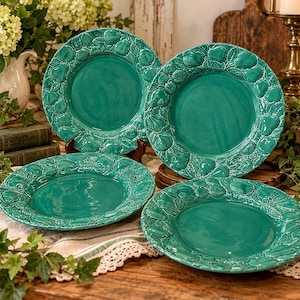 May include: A set of four round ceramic plates in a vibrant teal glaze. Each plate features a wide, embossed border decorated with a repeating pattern of raised pears, apples, and leaves, surrounding a smooth, plain center.