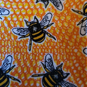 May include: A fabric featuring a repeating pattern of bees and honeycomb. The bees are black and yellow with white wings, set against a background of orange and yellow honeycomb shapes on a white background. The design is bright and cheerful.