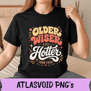 May include: Black t-shirt with the text "OLDER WISER AND HOTTER THAN EVER" in a retro font. The design features orange, yellow, and white lettering with decorative elements. The shirt is a crew neck.