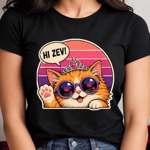 Könnte beinhalten: Schwarzes T-Shirt mit einer Illustration einer orangefarbenen Cartoon-Katze, die eine Sonnenbrille und eine Tiara trägt. Die Katze winkt mit einer Sprechblase mit der Aufschrift "HI ZEV!" vor einem Sonnenuntergangshintergrund.