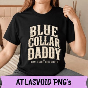 Peut inclure: T-shirt noir avec l'inscription "BLUE COLLAR DADDY" en police blanc cassé vieilli. Le texte "DIRTY HANDS, BUSY NIGHTS" est en dessous. Le t-shirt est à col rond.