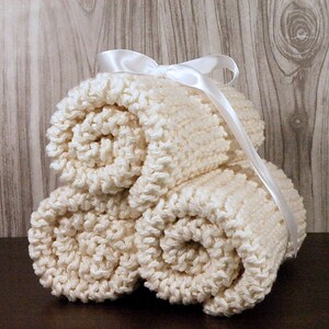 Pu&ograve; includere: Tre panni da bagno di colore crema a maglia sono arrotolati e legati insieme con un nastro di raso bianco.
