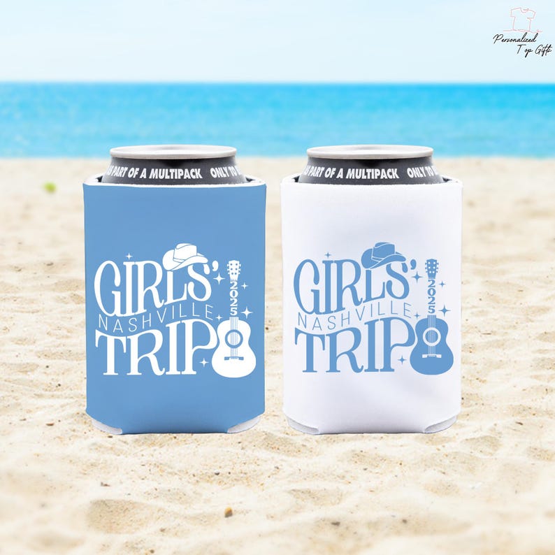 Pu&ograve; includere: Due porta-lattine, uno azzurro e uno bianco, con la scritta "GIRLS NASHVILLE TRIP" e una grafica di chitarra e cappello da cowboy. I porta-lattine sono su una spiaggia sabbiosa con l'oceano sullo sfondo.