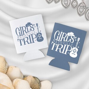 Pu&ograve; includere: Due portabicchieri, uno bianco e uno blu, con la scritta "GIRLS NASHVILLE TRIP 2025" in un carattere stilizzato. Il design include un cappello da cowboy, una chitarra e delle stelle. I portabicchieri sono progettati per mantenere le bevande fredde.