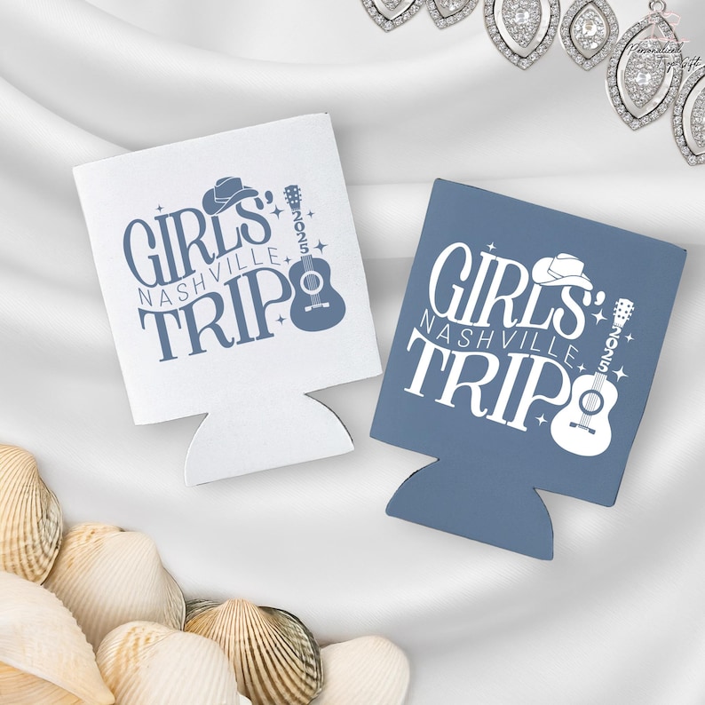 Pu&ograve; includere: Due portabicchieri, uno bianco e uno blu, con la scritta "GIRLS NASHVILLE TRIP 2025" in un carattere stilizzato. Il design include un cappello da cowboy, una chitarra e delle stelle. I portabicchieri sono progettati per mantenere le bevande fredde.
