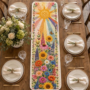 May include: A rectangular quilted table runner featuring a vibrant sunburst design at the top with radiating rays in yellow, orange, and blue, transitioning into a dense garden of colorful wildflowers, sunflowers, and butterflies on a white background.