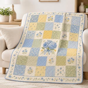May include: A patchwork quilt featuring a grid of squares in shades of light blue, yellow, and sage green. The design includes floral patterns, gingham checks, and stripes, with a central square displaying a large bouquet of blue hydrangeas.