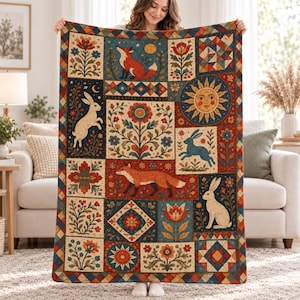 May include: A rectangular throw blanket featuring a patchwork design with illustrations of foxes, rabbits, a sun, and floral motifs in red, blue, and cream colors. The pattern includes geometric shapes and borders with a repeating diamond edge.