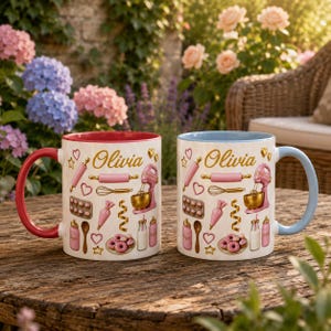 May include: Two ceramic mugs featuring the name Olivia in gold script, surrounded by illustrations of baking tools including a pink stand mixer, rolling pin, whisk, piping bag, and donuts. One mug has a red handle, the other a light blue handle.