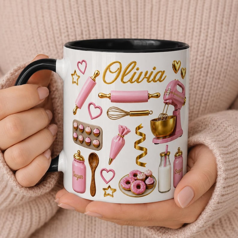 May include: A white ceramic mug with a black handle and rim, featuring the name Olivia in gold script. The design includes pink and gold baking illustrations: a stand mixer, rolling pin, whisk, piping bag, sugar jar, and a plate of pink donuts.