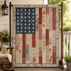 May include: A rectangular quilt featuring a patchwork design of the American flag. The blue canton displays cream-colored stars, while the stripes are composed of various fabric panels in red, cream, and blue with floral and striped patterns.