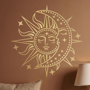 May include: A golden sun and moon wall decal with star accents. The sun and moon are intertwined, with closed eyes and detailed features. The decal is mounted on a brown wall, creating a celestial theme. The image also includes a lamp and vases.