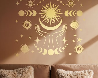 May include: Gold celestial wall decal with a sun, moon, and stars. The decal is on a brown wall above a brown couch with two fluffy pillows.