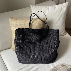 Può includere: Una borsa tote nera caratterizzata da una struttura intrecciata e testurizzata con un motivo a griglia. La borsa include due sottili tracolle nere lisce fissate al bordo superiore, offrendo un design funzionale per trasportare oggetti.