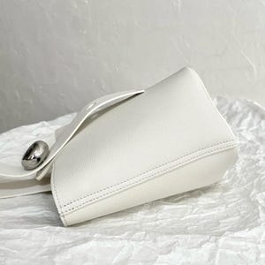 May include: A white leather bucket bag with a silver metal accent. The bag has a top handle and a detachable strap.