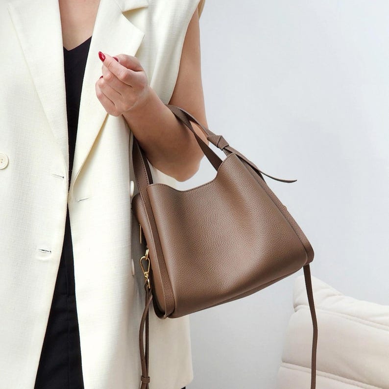 May include: A brown leather tote bag with a long strap. The bag has a top handle and a zipper closure.