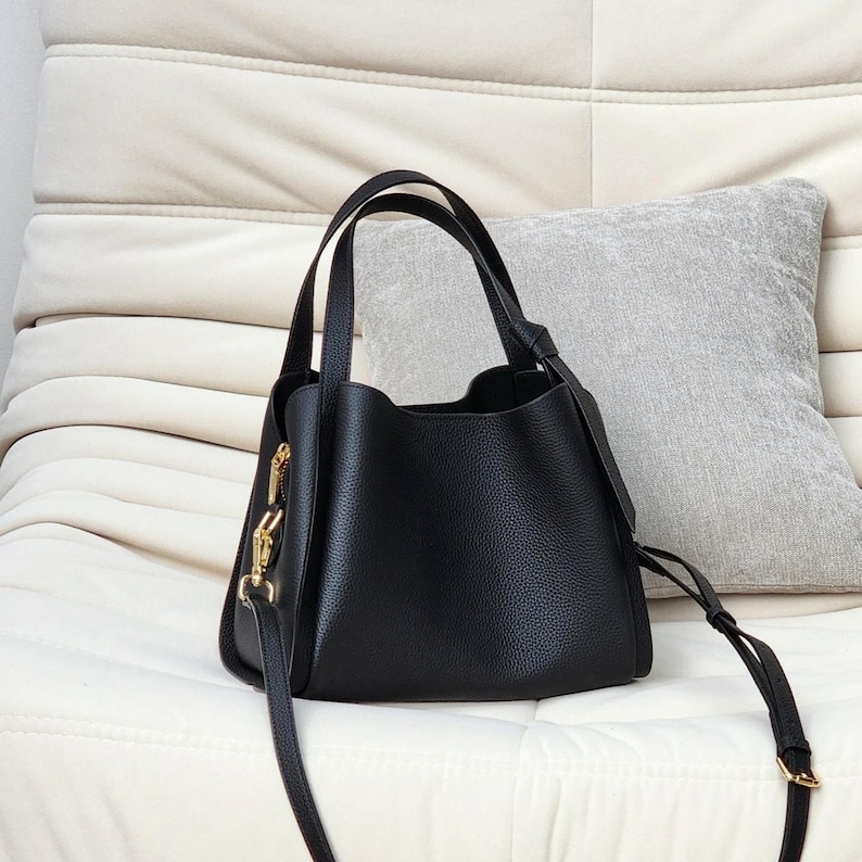 May include: A black leather tote bag with gold hardware and a long strap. The bag has a slouchy, casual look.