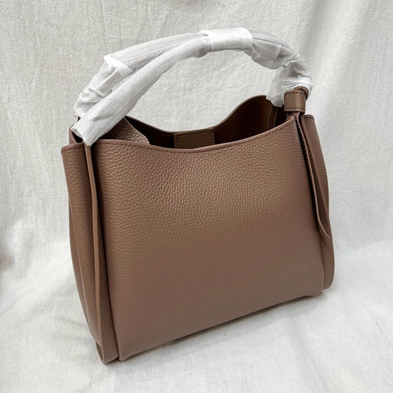 May include: A brown leather tote bag with a top handle and a flap closure. The bag has a textured finish and a slightly slouchy shape.