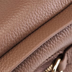May include: Close-up of a brown leather bag with a zipper detail. The leather has a textured, pebbled surface.