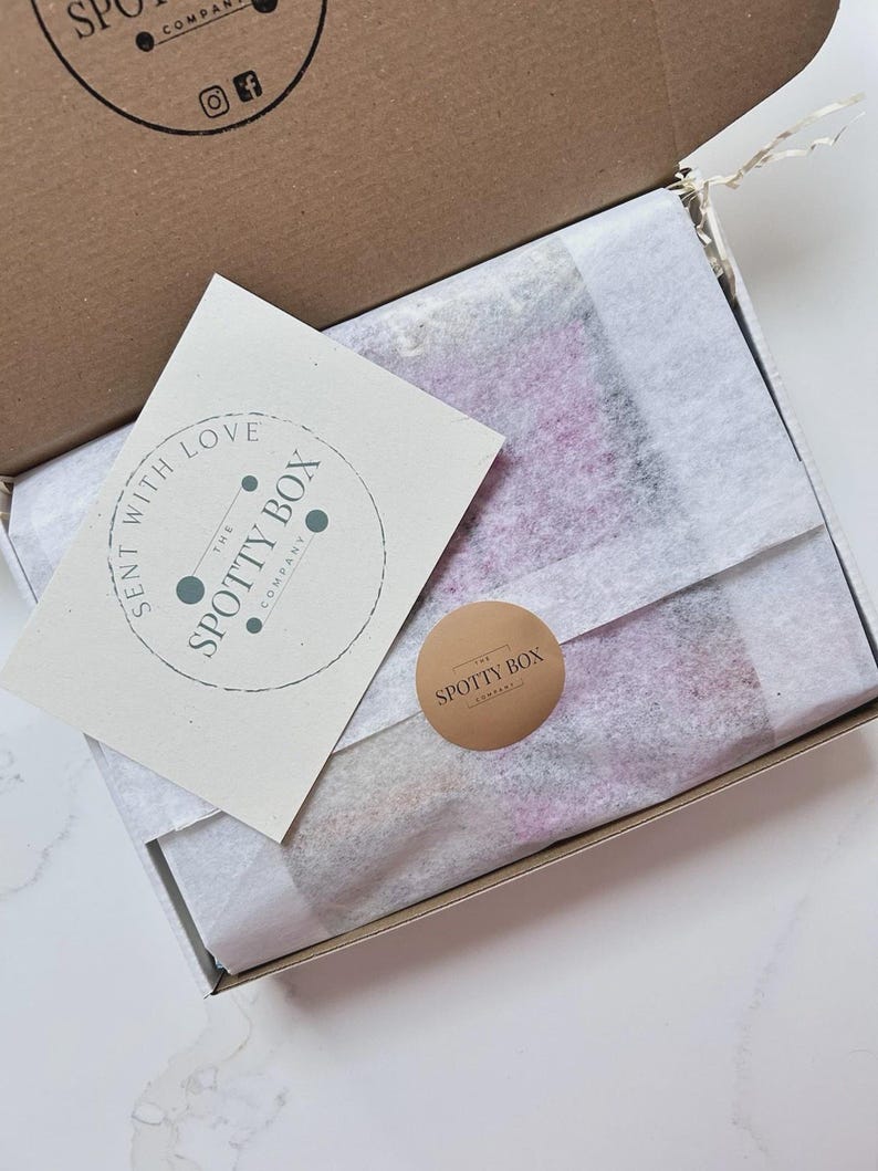 May include: An open cardboard box with a white interior, containing tissue paper and a product. A small card with the text "SENT WITH LOVE" and a circular logo is on the left. A round sticker with "SPOTTY BOX" is on the right.