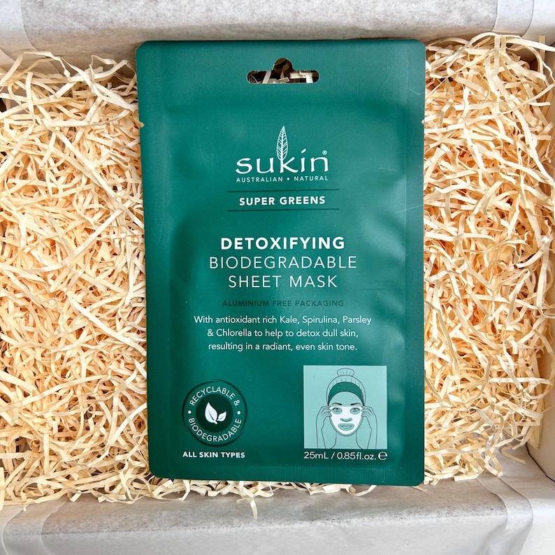 May include: A green Sukin Super Greens Detoxifying Biodegradable Sheet Mask package. The package includes the text "ALUMINIUM FREE PACKAGING" and "25ml / 0.85fl.oz. e". The mask is designed for all skin types.